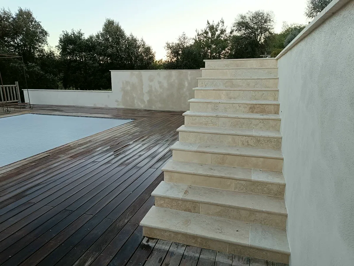 Escalier en pierre descendant vers une plage de piscine et une terrasse en bois